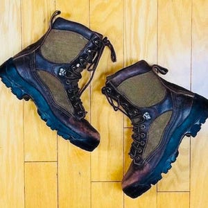 May include: A pair of brown leather hiking boots with green canvas accents and laces. The boots have a rugged outsole and a lace-up closure.