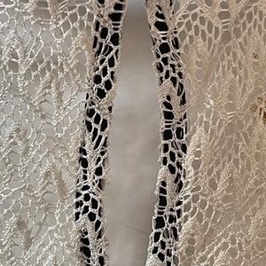 May include: Close-up of a white lace fabric with a black trim. The fabric has a delicate pattern and is sewn together with a black thread.