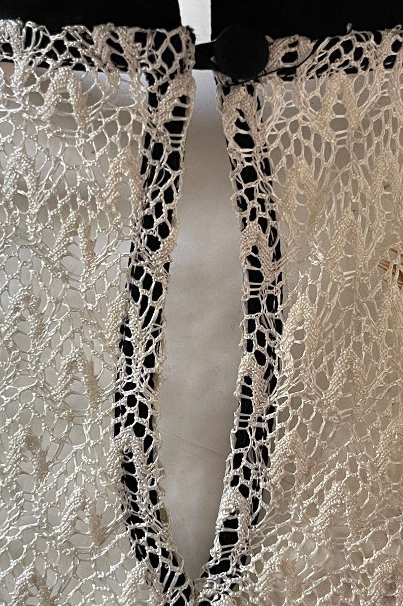 May include: Close-up of a white lace fabric with a black trim. The fabric has a delicate pattern and is sewn together with a black thread.