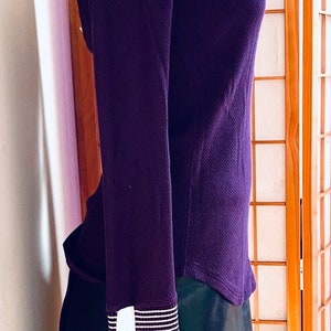 May include: A long-sleeved, purple thermal shirt with white striped cuffs. The shirt is on a white mannequin and is displayed against a wooden screen.