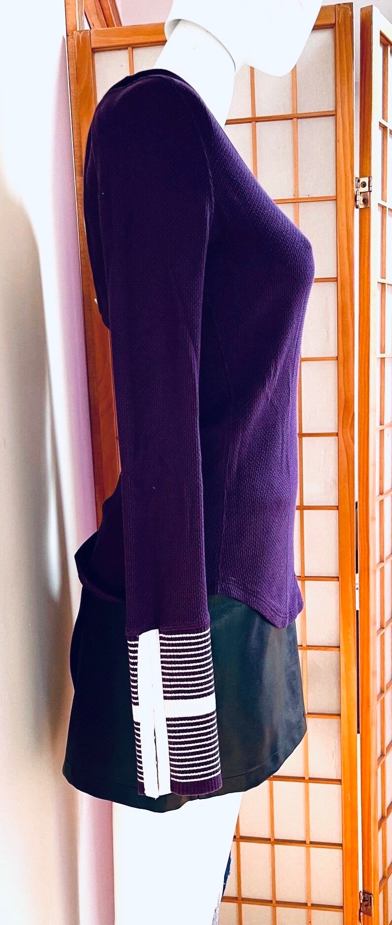 May include: A long-sleeved, purple thermal shirt with white striped cuffs. The shirt is on a white mannequin and is displayed against a wooden screen.