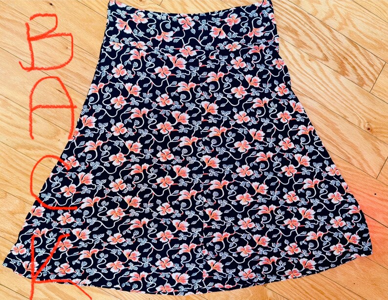May include: A-line skirt with a navy blue background and a repeating floral pattern in coral and white. The skirt is made of a lightweight fabric and has a comfortable waistband. The skirt is suitable for casual wear.