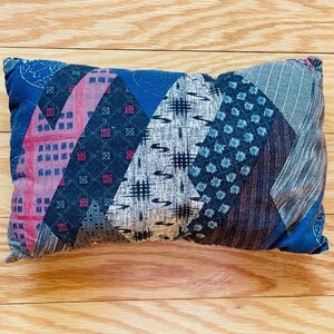 May include: A blue and pink patchwork pillow with a geometric pattern. The pillow is made of different fabrics with various textures and designs.