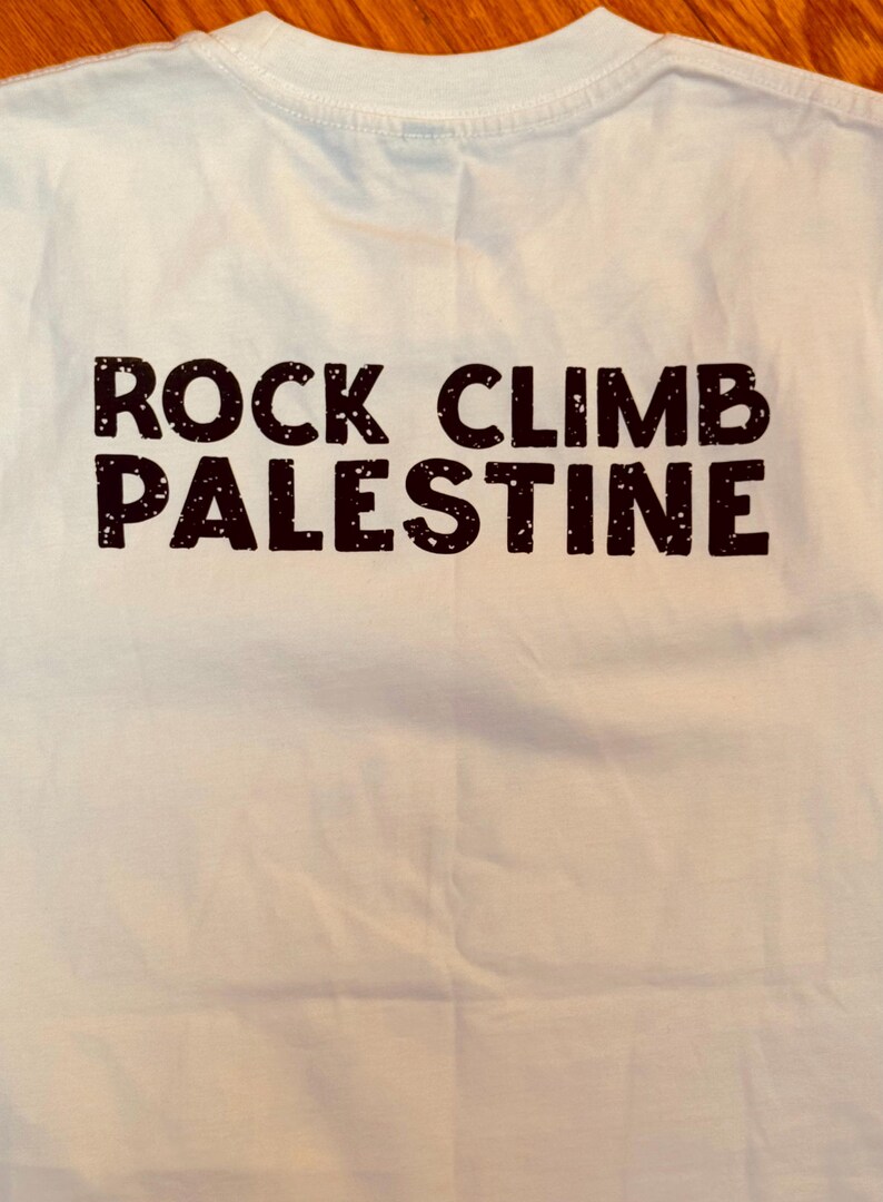 Puede incluir: Camiseta blanca con texto negro que dice "ROCK CLIMB PALESTINE".