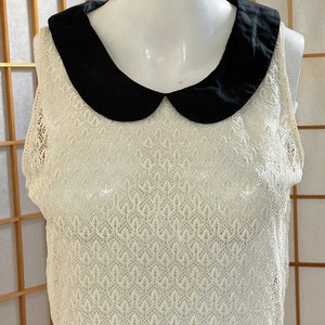 May include: A white crochet sleeveless top with a black peter pan collar.
