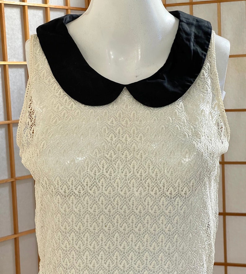 May include: A white crochet sleeveless top with a black peter pan collar.