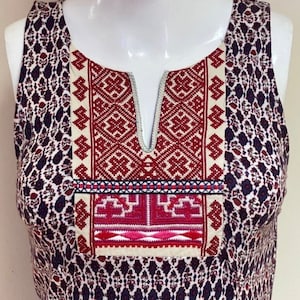 May include: A sleeveless dress with a white and red embroidered neckline. The dress has a geometric pattern in shades of blue, red, and white.