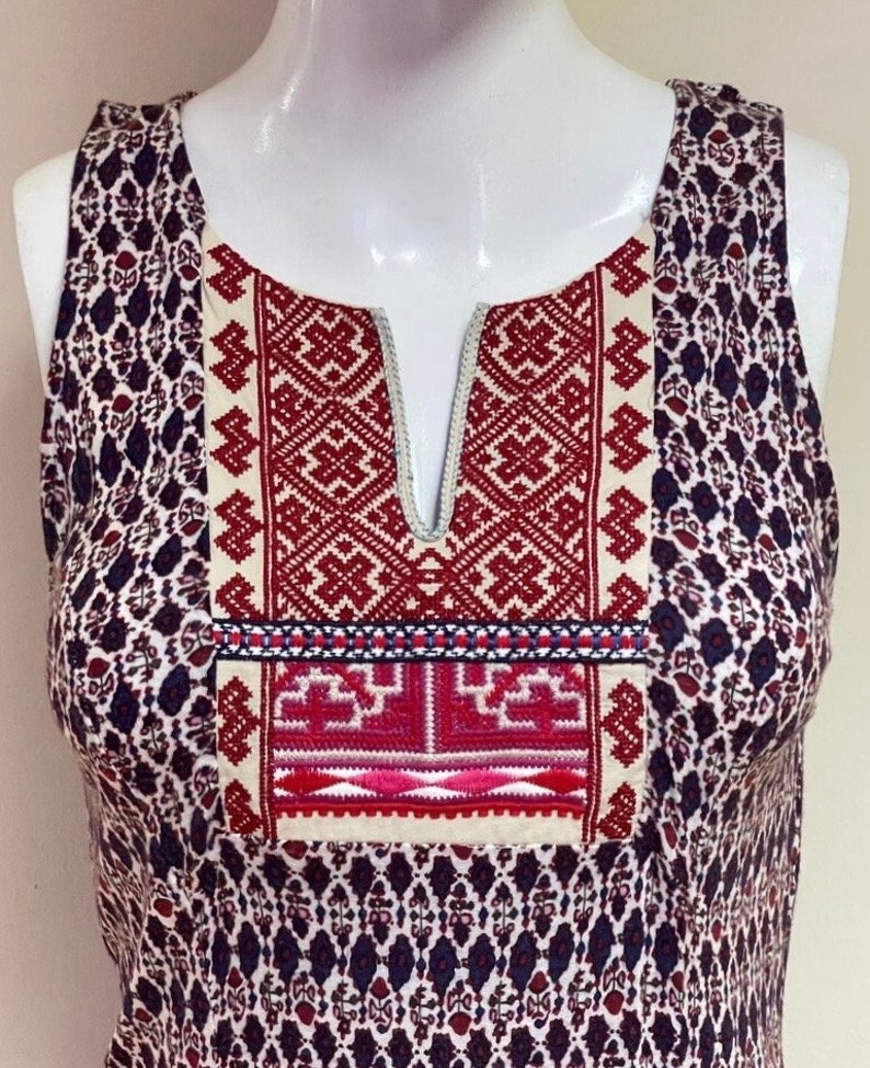May include: A sleeveless dress with a white and red embroidered neckline. The dress has a geometric pattern in shades of blue, red, and white.