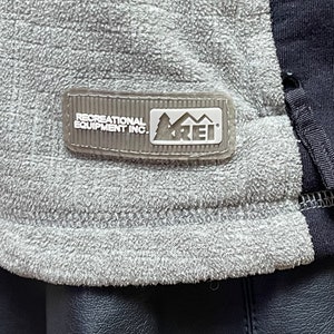 May include: A gray fleece jacket with a black zipper and a white REI logo patch that reads "Recreational Equipment Inc."