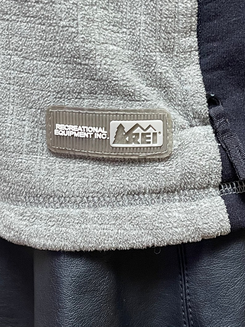 May include: A gray fleece jacket with a black zipper and a white REI logo patch that reads "Recreational Equipment Inc."