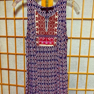 May include: A sleeveless, blue and white patterned dress with a red and white embroidered design on the front. The dress has a scoop neck and a relaxed fit.