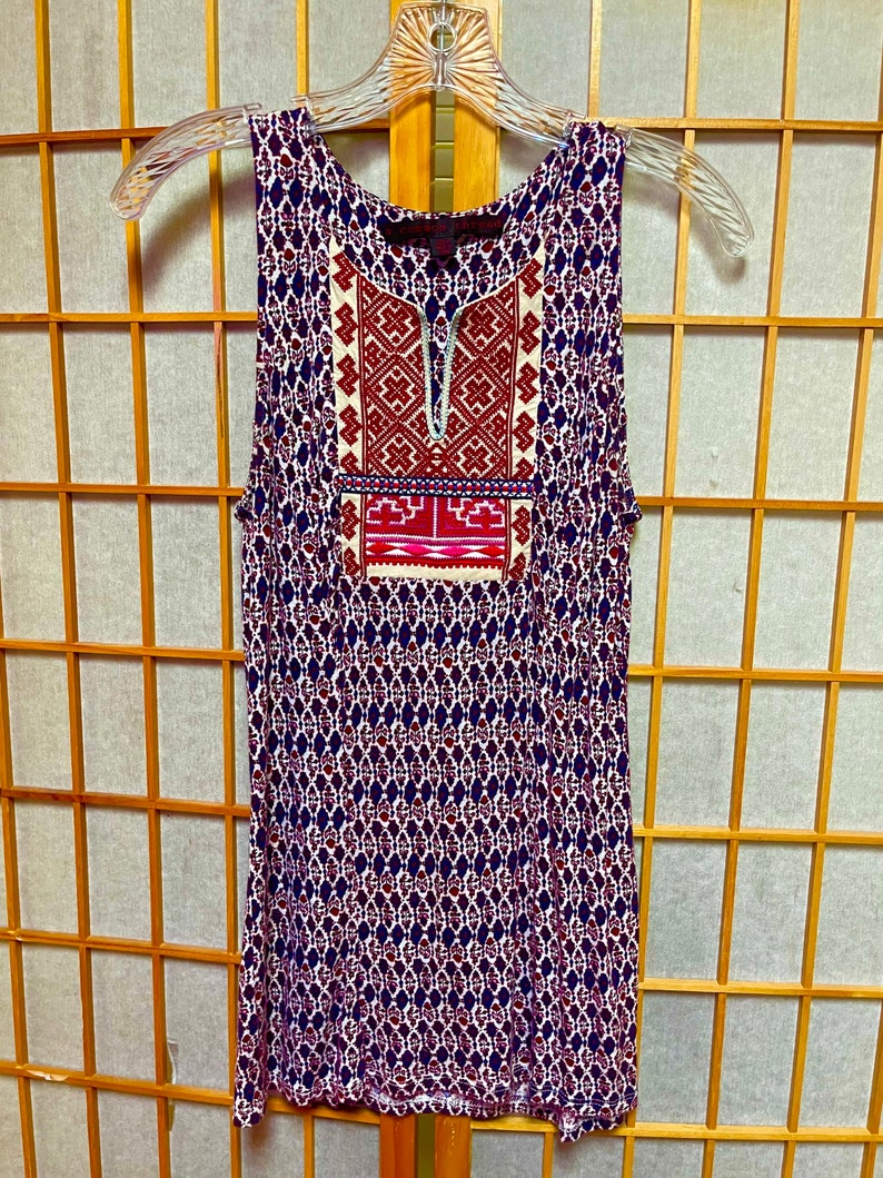 May include: A sleeveless, blue and white patterned dress with a red and white embroidered design on the front. The dress has a scoop neck and a relaxed fit.