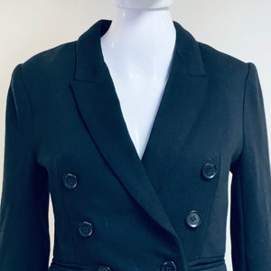 Puede incluir: Una chaqueta negra de doble botonadura con cuatro botones. La chaqueta tiene un corte clásico y entallado.