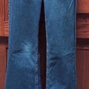 May include: High-waisted, dark wash denim jeans with a button-up fly. The jeans have a flared leg design and classic five-pocket styling. The jeans are made of a sturdy denim material.