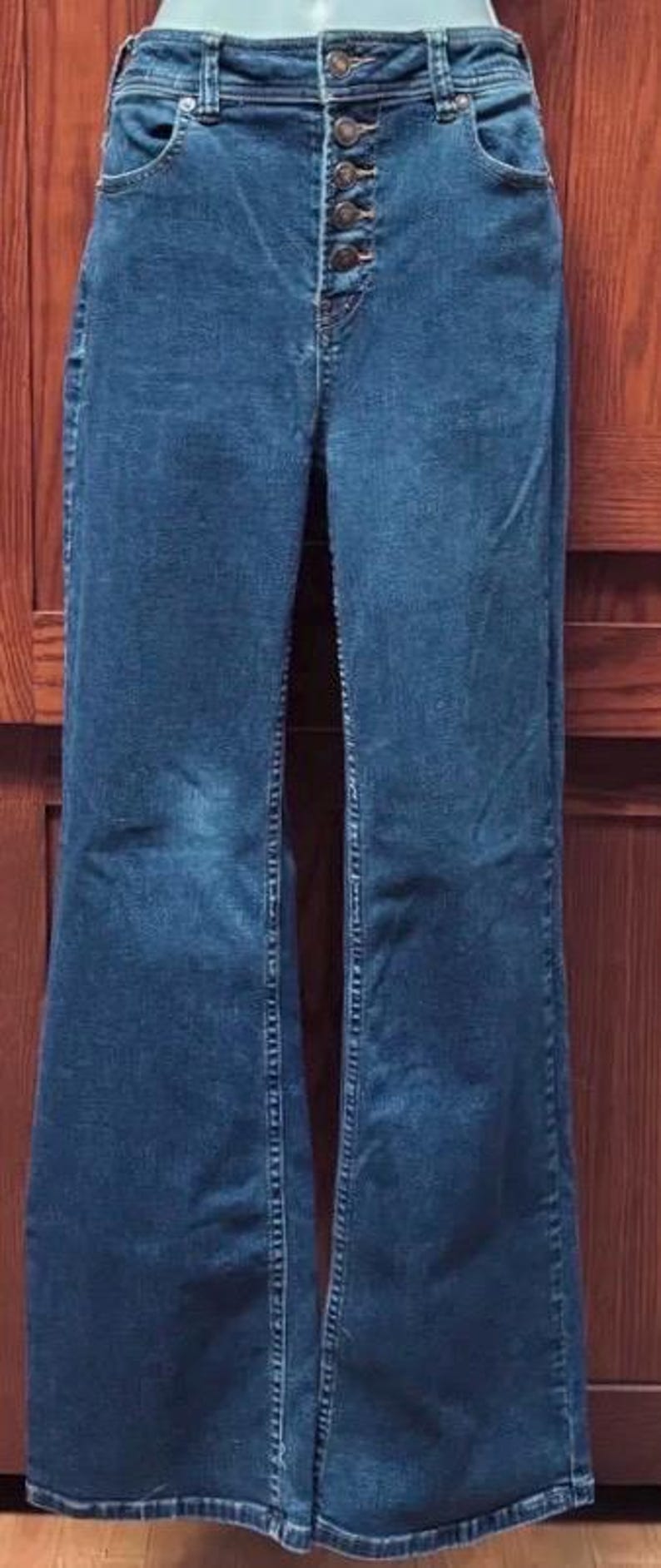 May include: High-waisted, dark wash denim jeans with a button-up fly. The jeans have a flared leg design and classic five-pocket styling. The jeans are made of a sturdy denim material.