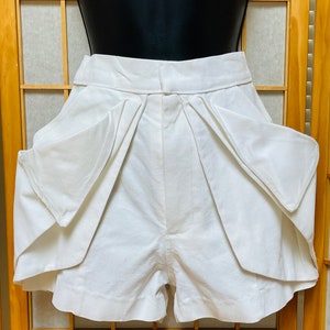 May include: White linen shorts with large, pleated pockets. The shorts have a high waist and a relaxed fit.