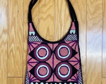 May include: A black and purple embroidered handbag with a geometric pattern of pink circles and white accents. The bag has a single strap.
