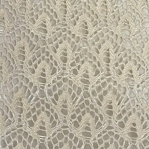 May include: A close-up of a white crocheted fabric with a delicate, intricate pattern. The fabric has a soft, airy texture and a subtle sheen.
