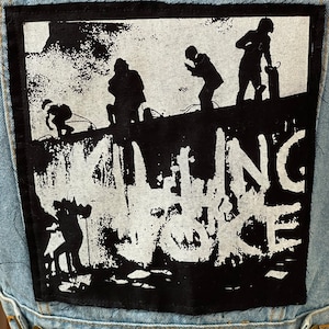 Pode incluir: Um remendo preto e branco com o nome de uma banda, "Falling Voice", impresso em branco. O remendo apresenta a silhueta de quatro pessoas em pé em uma parede.