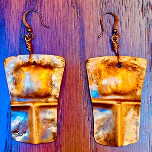 Peut inclure: Une paire de boucles d'oreilles dorées avec un design en métal martelé. Les boucles d'oreilles sont de forme rectangulaire et ont un bord légèrement incurvé. Les boucles d'oreilles sont suspendues à un simple crochet en fil.