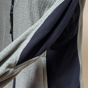 May include: Gray fleece jacket with black panels on the sides and a zipper closure. The jacket has a REI logo on the lower left side.