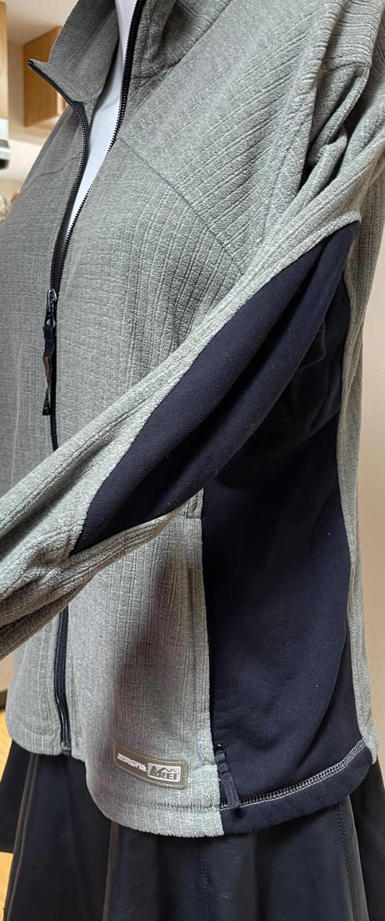 May include: Gray fleece jacket with black panels on the sides and a zipper closure. The jacket has a REI logo on the lower left side.