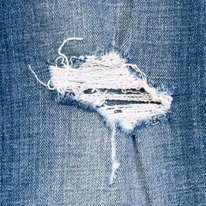 K&ouml;nnte beinhalten: Nahaufnahme eines blauen Jeansstoffes mit einem kleinen, ausgefransten Loch in der Mitte.