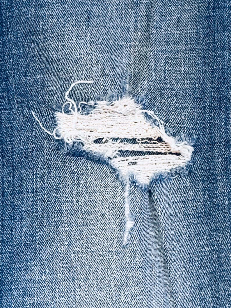 K&ouml;nnte beinhalten: Nahaufnahme eines blauen Jeansstoffes mit einem kleinen, ausgefransten Loch in der Mitte.