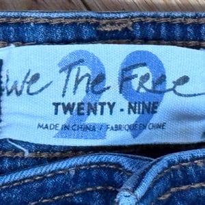 May include: Close-up of a blue denim garment with a white label. The label reads "We The Free" above the number "29" in a stylized font. Below, it says "TWENTY - NINE" and "MADE IN CHINA / FABRIQU&Eacute; EN CHINE".