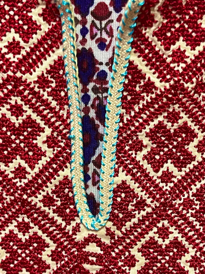 May include: Close-up of a red and white embroidered fabric with a blue and white trim. The fabric has a geometric pattern.