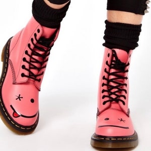 May include: Pink leather boots with black laces and a black smiley face with a tongue sticking out on the toe.