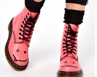 May include: Pink leather boots with black laces and a black smiley face with a tongue sticking out on the toe.