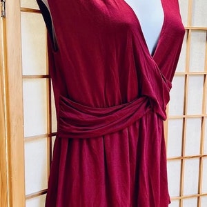Pu&ograve; includere: Una camicetta senza maniche color borgogna con scollo a V e vita arricciata.