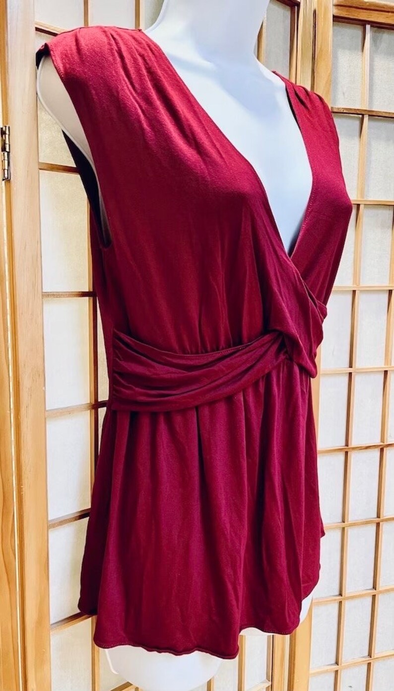 Pu&ograve; includere: Una camicetta senza maniche color borgogna con scollo a V e vita arricciata.