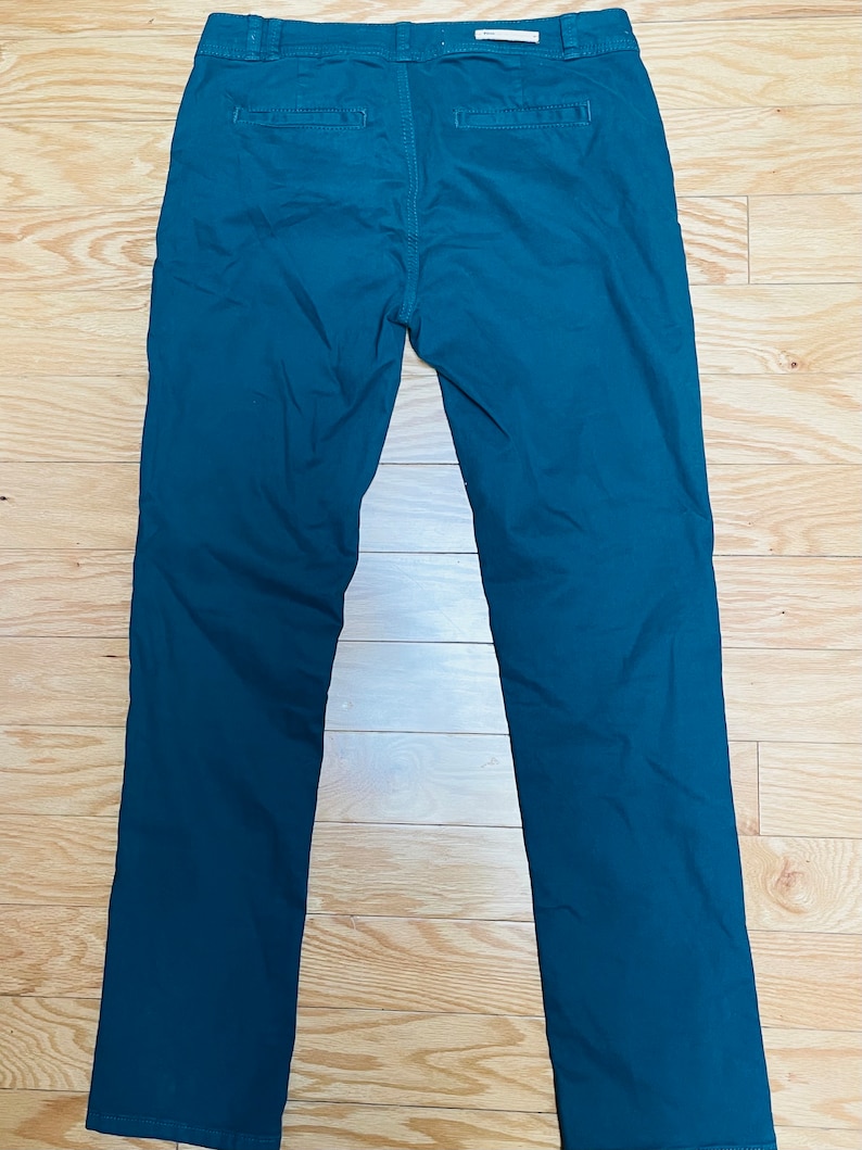 Puede incluir: Pantalones de color verde azulado con dise&ntilde;o de pierna recta. La parte trasera muestra los bolsillos y la cintura. Los pantalones est&aacute;n hechos de una tela de color liso y parecen ser de estilo casual. La longitud del pantal&oacute;n es de unos 100 cm.