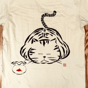 May include: A white t-shirt with a black and white illustration of a tiger with a curled tail, looking at a goldfish in a bowl. The illustration is in a Japanese style.