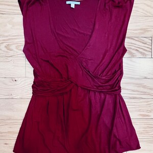 Pu&ograve; includere: Una blusa senza maniche color borgogna con scollo a V e un dettaglio annodato in vita.