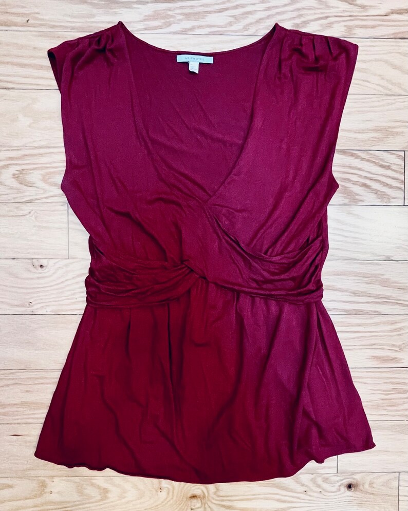 Pu&ograve; includere: Una blusa senza maniche color borgogna con scollo a V e un dettaglio annodato in vita.