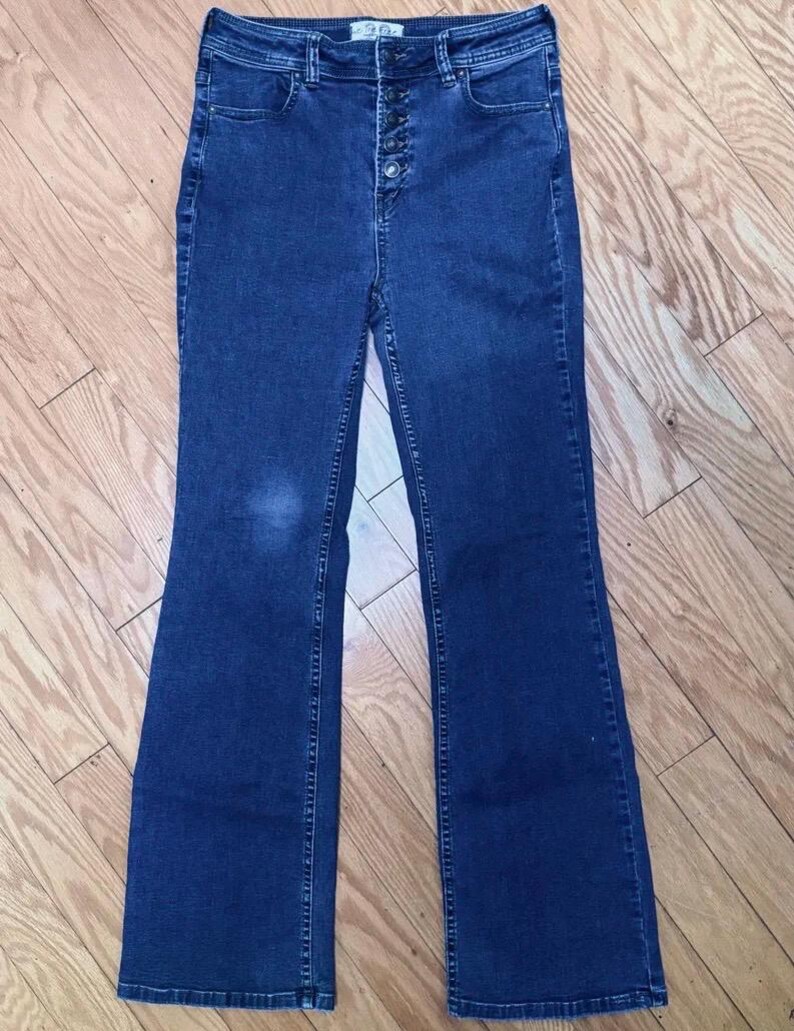 May include: Dark wash denim flare jeans with a high waist and button fly. The jeans have a classic five-pocket design and a flared leg opening. The jeans are made of a medium-weight denim fabric.