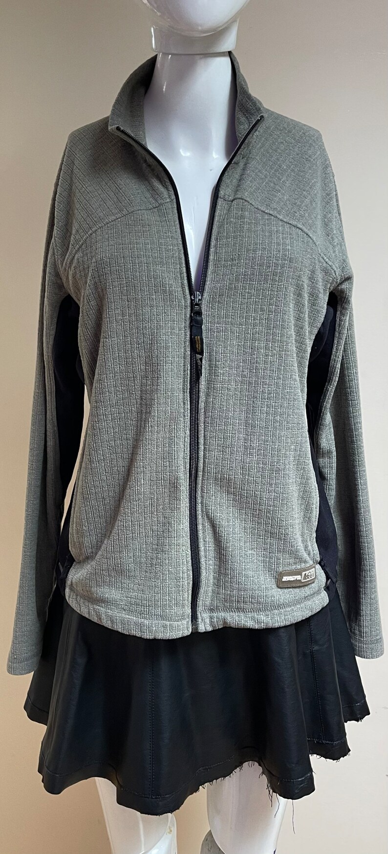 May include: A gray zippered jacket with black accents on the sleeves. The jacket has a ribbed texture and a small logo on the bottom right side.