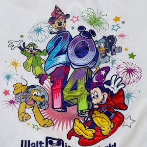 K&ouml;nnte beinhalten: Wei&szlig;er Hoodie mit einem bunten gestickten Design mit Mickey Mouse, Minnie Mouse, Goofy, Pluto und Donald Duck. Das Design beinhaltet das Jahr 2014 und Feuerwerk. Der Text "Walt Disney World" ist unter dem Design gestickt.