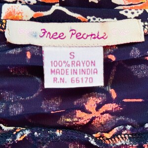 May include: Close-up of a garment with a floral pattern in orange and white on a dark blue background. The label reads "Free People" and includes details about the fabric composition and origin.
