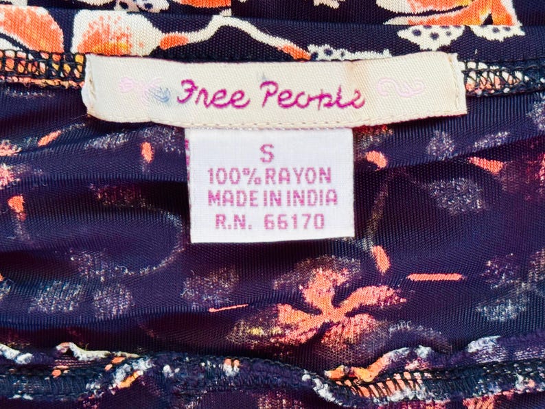 May include: Close-up of a garment with a floral pattern in orange and white on a dark blue background. The label reads "Free People" and includes details about the fabric composition and origin.