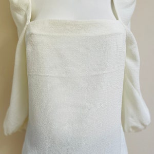 May include: A white, textured, square-neck blouse with puffed sleeves.