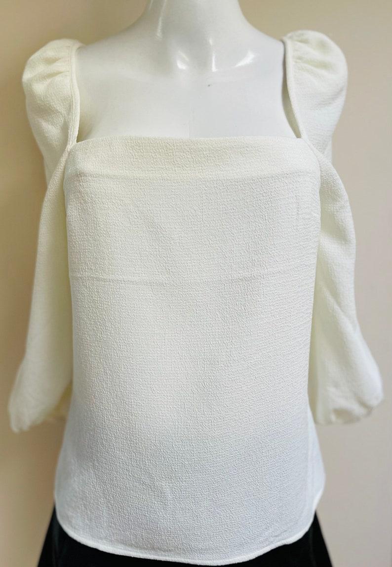 May include: A white, textured, square-neck blouse with puffed sleeves.