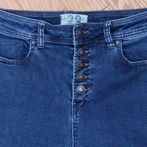 May include: Close-up of dark blue denim jeans with a button fly. The jeans have a high waist and pockets on the front and back. The brand name "We The Free" is visible on the waistband.