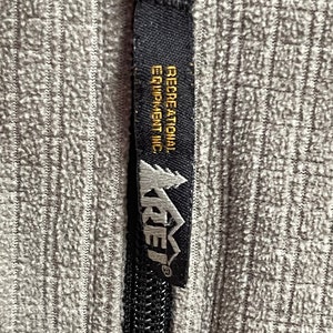 May include: A black zipper pull with a black and white label that reads "Recreational Equipment Inc." and a white logo that reads "REI" with a mountain graphic.