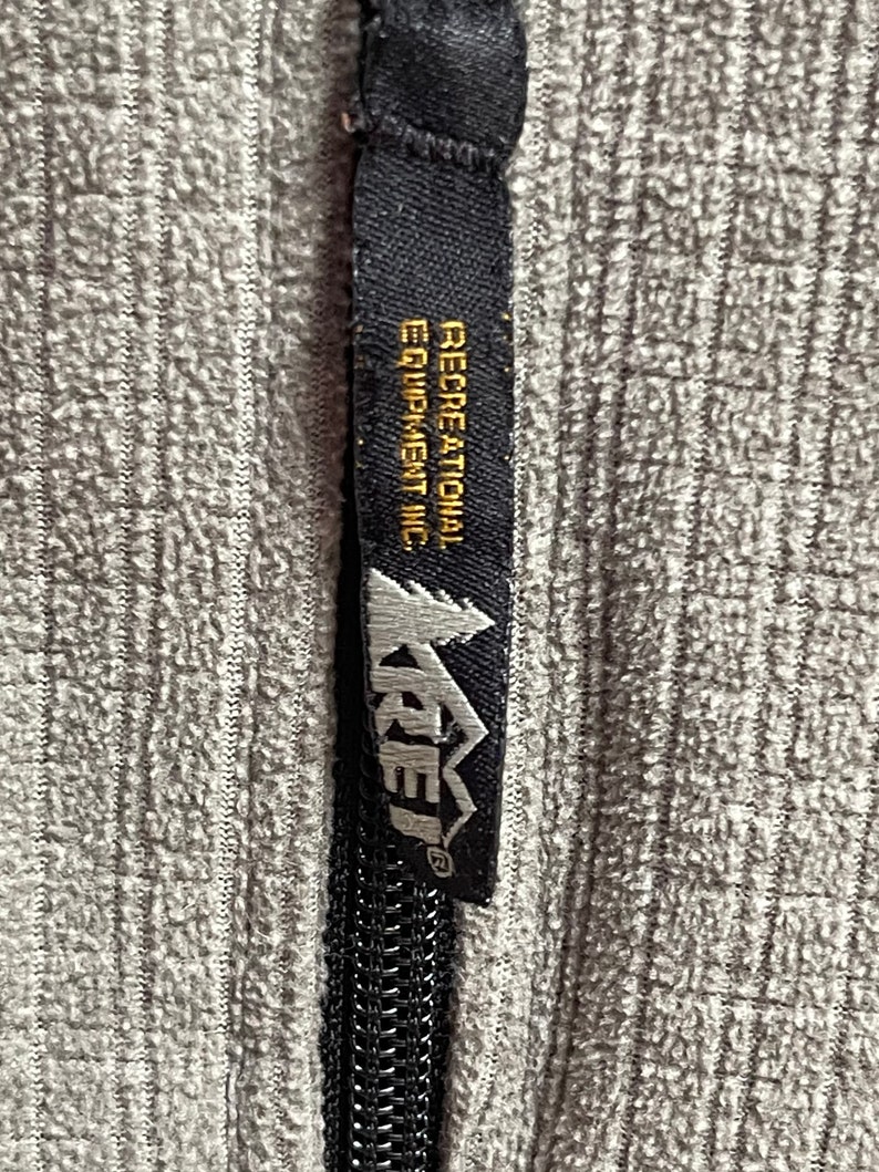 May include: A black zipper pull with a black and white label that reads "Recreational Equipment Inc." and a white logo that reads "REI" with a mountain graphic.