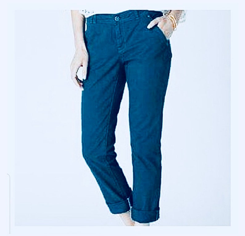 Puede incluir: Pantalones de color verde azulado oscuro con cierre de bot&oacute;n y bolsillos. Los pantalones tienen una pernera recta y est&aacute;n doblados en los tobillos. La tela es lisa y de color s&oacute;lido.