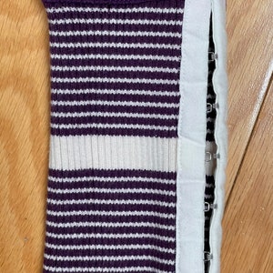May include: Purple and white striped sweater cuff with a white fabric strip and metal snaps along the side.